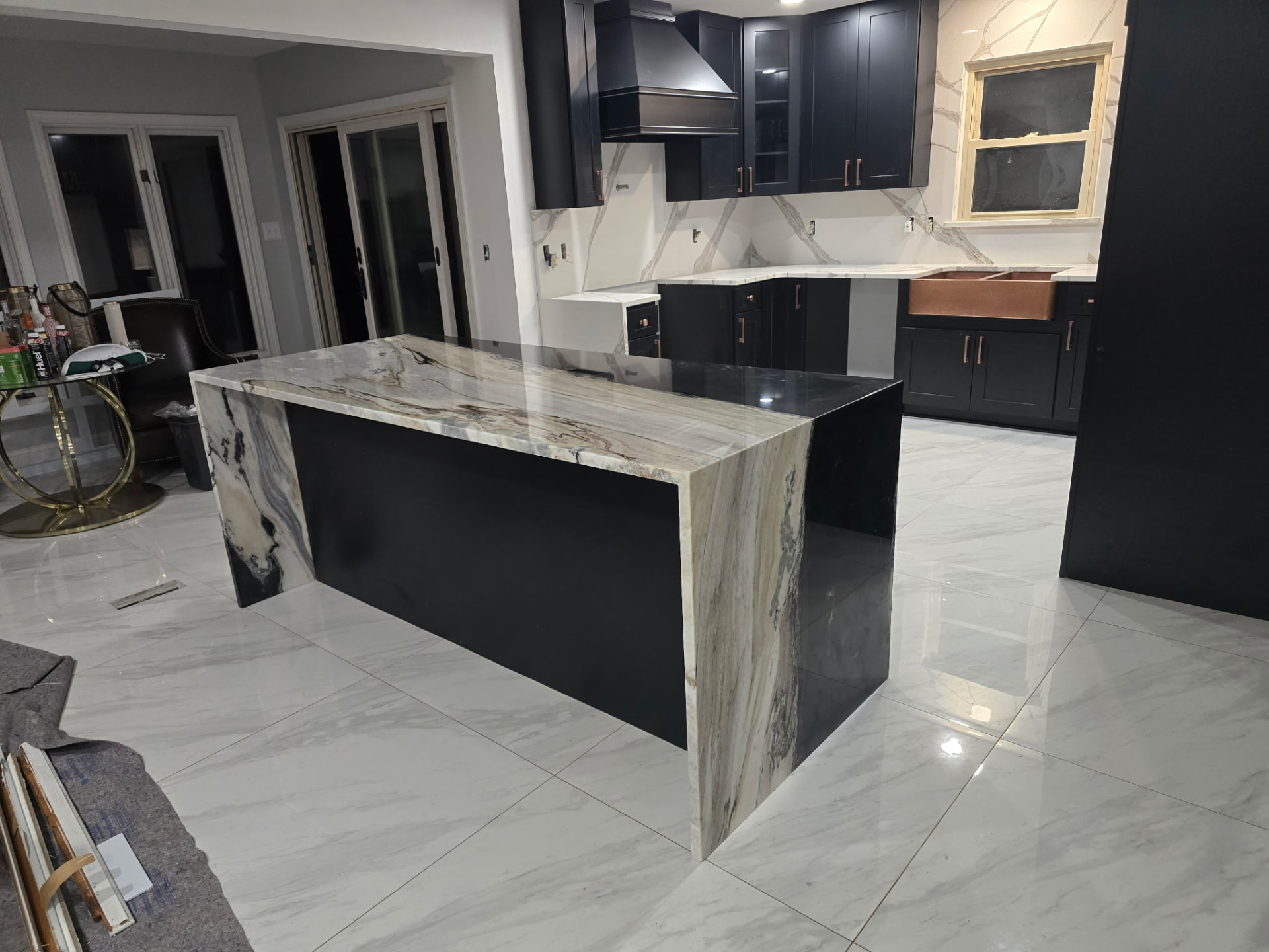 Black cabinetry kitchen with stone waterfall island and copper sink